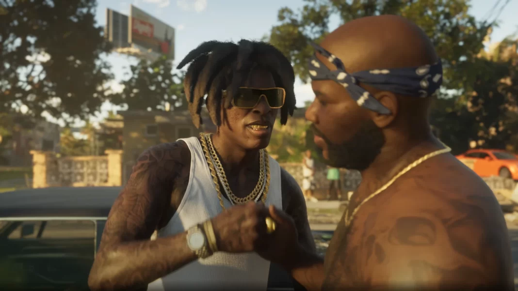 Um homem negro jovem, usando tranças afro, camisa regata branca e joias, cumprimenta outro homem negro, calvo, sem camisa, que usa um lenço na cabeça e também ostenta joias. Ambos têm tatuagens. O primeiro sorri, mostrando grillz brilhantes nos dentes.