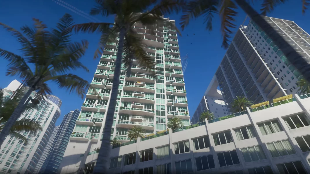 Um grande prédio em GTA 6, de cor clara, com varandas e palmeiras em frente, sobre um céu azul, visto do ponto de vista da rua logo abaixo.