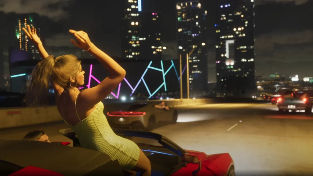 Uma mulher de vestido amarelo brilhante dança em pé no banco de um carro vermelho conversível, que segue por uma via da cidade noturna, com grandes prédio iluminados ao fundo.