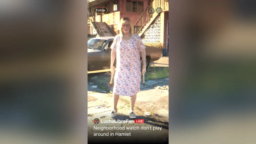 Idosa loira usando vestido ou camisola estampada segura um martelo em cada mão, olhando com expressão séria para o interlocutor que a filma. Ela diz "Olhe quem voltou" em tom ameaçador.
